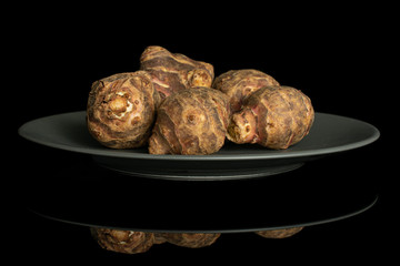 Group of five whole fresh brown jerusalem artichoke on gray ceramic plate isolated on black glass