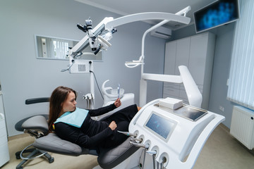 Female patient sits it dental chair and looking to the mirror. Modern dental office. Stomatology concept. Medicine, dentistry and health care concept. Oral care.