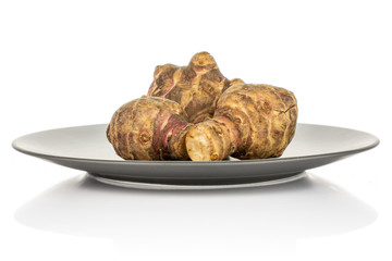 Group of three whole fresh brown jerusalem artichoke on gray ceramic plate isolated on white background