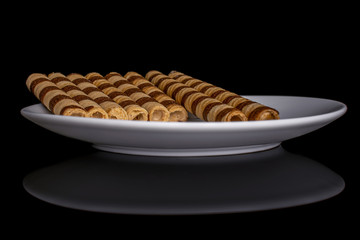 Group of eight whole crunchy beige hazelnut rolled wafer biscuit on white ceramic plate isolated on black glass