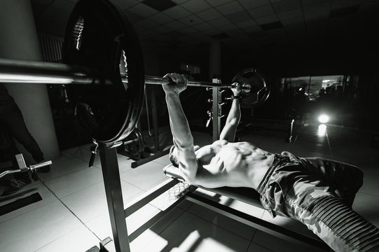 Fit young man lifting barbells doing workout at a gym. Sport, fitness, weightlifting, bodybuilding, training, athlete, workout exercises concept. View from the side. Bench press.