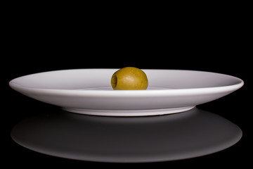 One whole pitted green olive on white ceramic plate isolated on black glass