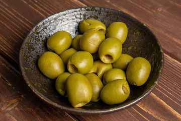 Lot of whole pitted green olive in dark ceramic bowl on brown wood