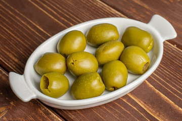 Lot of whole pitted green olive in white oval ceramic bowl on brown wood