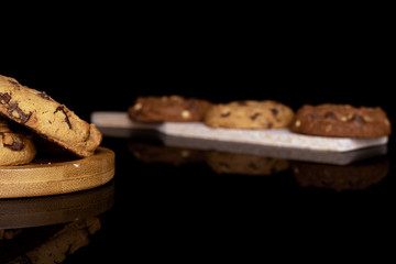 Group of five whole sweet brown cookie on wooden cutting board on round bamboo coaster isolated on black glass