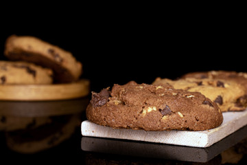 Group of five whole sweet brown cookie on wooden cutting board on round bamboo coaster isolated on black glass
