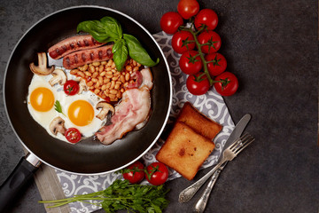 English breakfast. Fried eggs, sausages, bacon, beans, toasts, tomatoes on stone table. Top view with copy space