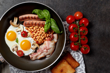 English breakfast. Fried eggs, sausages, bacon, beans, toasts, tomatoes on stone table. Top view with copy space