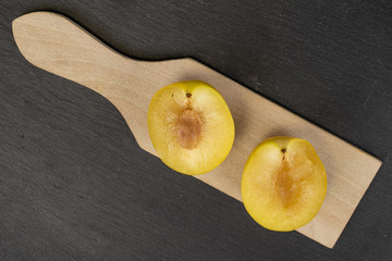 Group of two halves of fresh yellow plum on wooden cutting board flatlay on grey stone