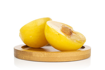 Group of two halves of fresh yellow plum on round bamboo coaster isolated on white background