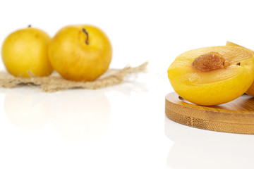 Group of two whole one half of fresh yellow plum on round bamboo coaster with jute fabric isolated on white background