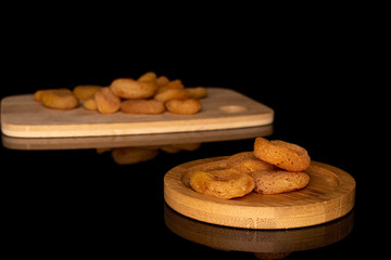Lot of whole dried orange apricot on bamboo cutting board on round bamboo coaster isolated on black glass
