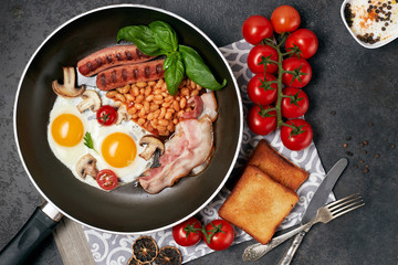 English breakfast. Fried eggs, sausages, bacon, beans, toasts, tomatoes on stone table. Top view with copy space