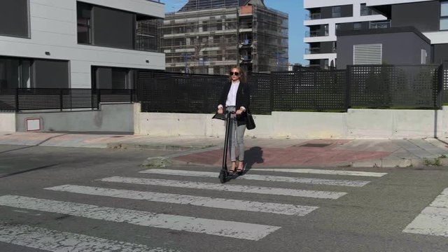 Slow motion of fashion businesswoman crossing the street on electric scooter on the sidewalk