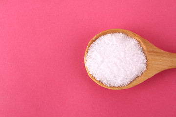 Salt on a wooden spoon on a pink background.
