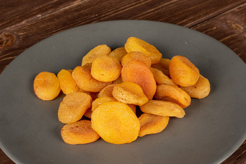 Lot of whole dried orange apricot on gray ceramic plate on brown wood
