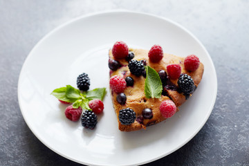 Piece of pie with blueberries, raspberry and mint for dessert on a white plate. Pieces of delicious homemade cake on a background