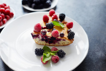 Piece of pie with blueberries, raspberry and mint for dessert on a white plate. Pieces of delicious homemade cake on a background
