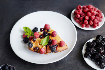 Piece of pie with blueberries, raspberry and mint for dessert on a white plate. Pieces of delicious homemade cake on a background