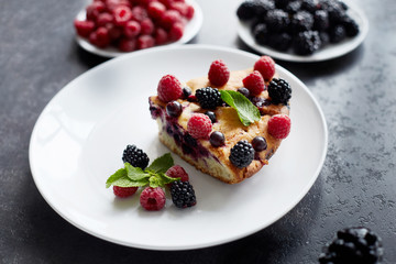 Piece of pie with blueberries, raspberry and mint for dessert on a white plate. Pieces of delicious homemade cake on a background