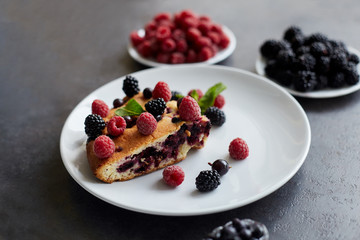 Piece of pie with blueberries, raspberry and mint for dessert on a white plate. Pieces of delicious homemade cake on a background
