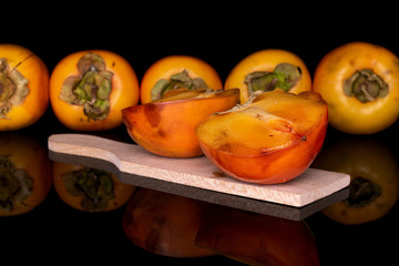 Group of five whole two halves of sweet orange persimmon on wooden cutting board isolated on black glass