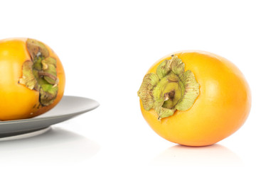 Group of two whole sweet orange persimmon on gray ceramic plate isolated on white background