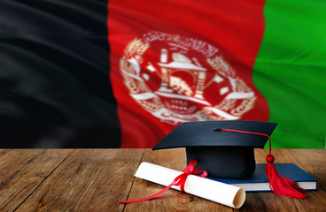 Afghanistan education concept. Graduation cap and diploma on wooden table, national flag...