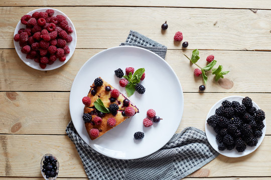 Piece of pie with blueberries, raspberry and mint for dessert on a white plate, napkin. Pieces of delicious homemade cake on a wooden boards background