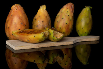 Group of four whole two halves of prickly green opuntia on wooden cutting board isolated on black glass