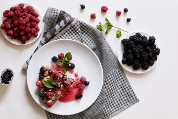 Piece of pie with blueberries, raspberry and mint for dessert on a white plate. Pieces of delicious homemade cake on a background