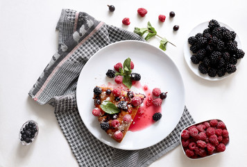Piece of pie with blueberries, raspberry and mint for dessert on a white plate. Pieces of delicious homemade cake on a background