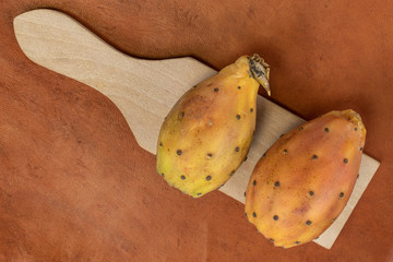 Group of two whole prickly green opuntia on wooden cutting board flatlay on cognac leather