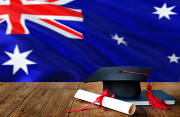 Australia education concept. Graduation cap and diploma on wooden table, national flag background. Succesful student.