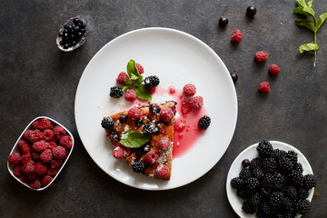 Piece of pie with blueberries, raspberry and mint for dessert on a white plate. Pieces of delicious homemade cake on a background