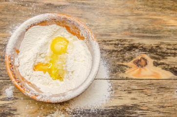 brown bowl of flour and egg stands on a wooden background, top view, copy space