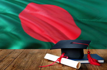 Bangladesh education concept. Graduation cap and diploma on wooden table, national flag background. Succesful student.