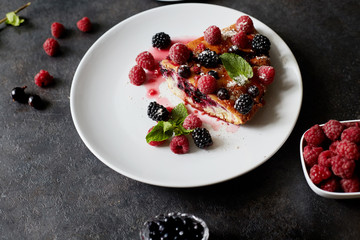 Piece of pie with blueberries, raspberry and mint for dessert on a white plate. Pieces of delicious homemade cake on a background