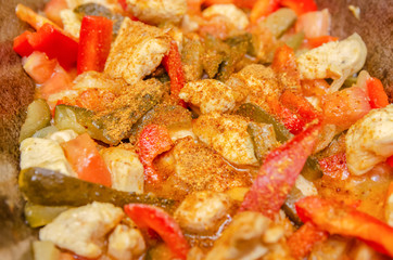 In the cauldron fried pieces of chicken, red bell pepper, tomatoes, pickles, white onions and all sprinkled with seasonings. Background of delicious food: meat, vegetables