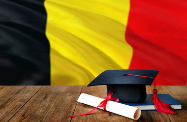 Belgium education concept. Graduation cap and diploma on wooden table, national flag background....