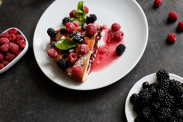 Piece of pie with blueberries, raspberry and mint for dessert on a white plate. Pieces of delicious homemade cake on a background