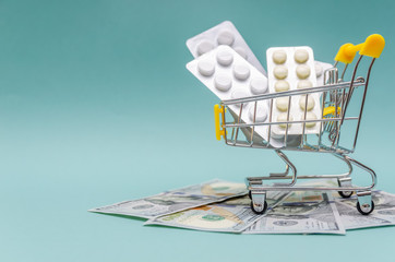 yellow shopping cart with pills stands on dollar bills on a blue background close-up. Concept of...
