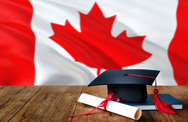 Canada education concept. Graduation cap and diploma on wooden table, national flag background....