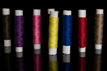 Group of eight whole arranged sewing thread spool isolated on black glass