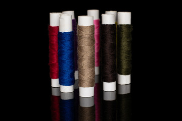 Group of eight whole upright sewing thread spool isolated on black glass