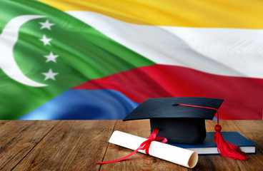Comoros education concept. Graduation cap and diploma on wooden table, national flag background....