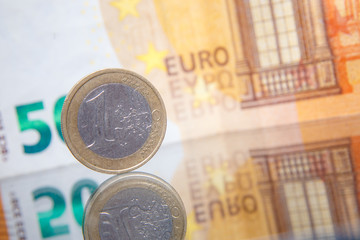 Macro photo of a coin in 1 euro on a blurred background banknote in 50 euro. Reflection of the coin on the glass table. Very small depth of field.