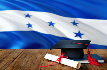Honduras education concept. Graduation cap and diploma on wooden table, national flag background....