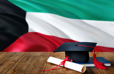 Kuwait education concept. Graduation cap and diploma on wooden table, national flag background. Succesful student.