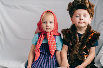 Beautiful couple of lovely children in bear costume and russian cartoon clothes sitting on bed with funny faces. Soft focus portrait of little children in costumes